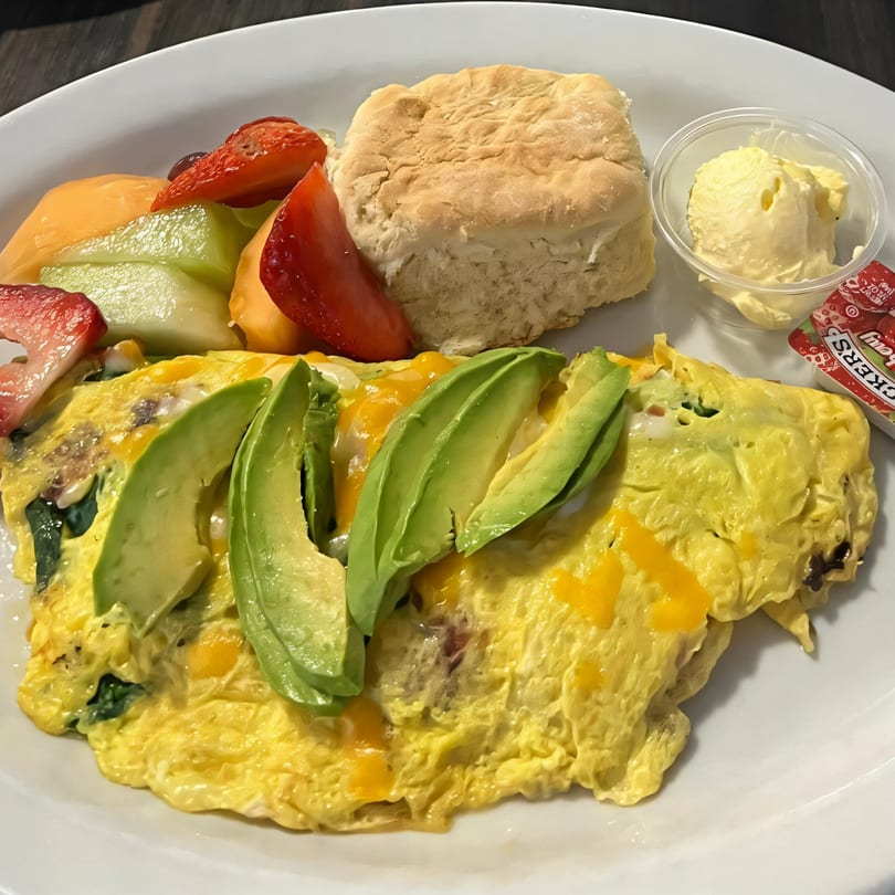 A Jerry's Cafe omelet with avocado, cheese, and spinach, served with a biscuit, fruit, and butter.