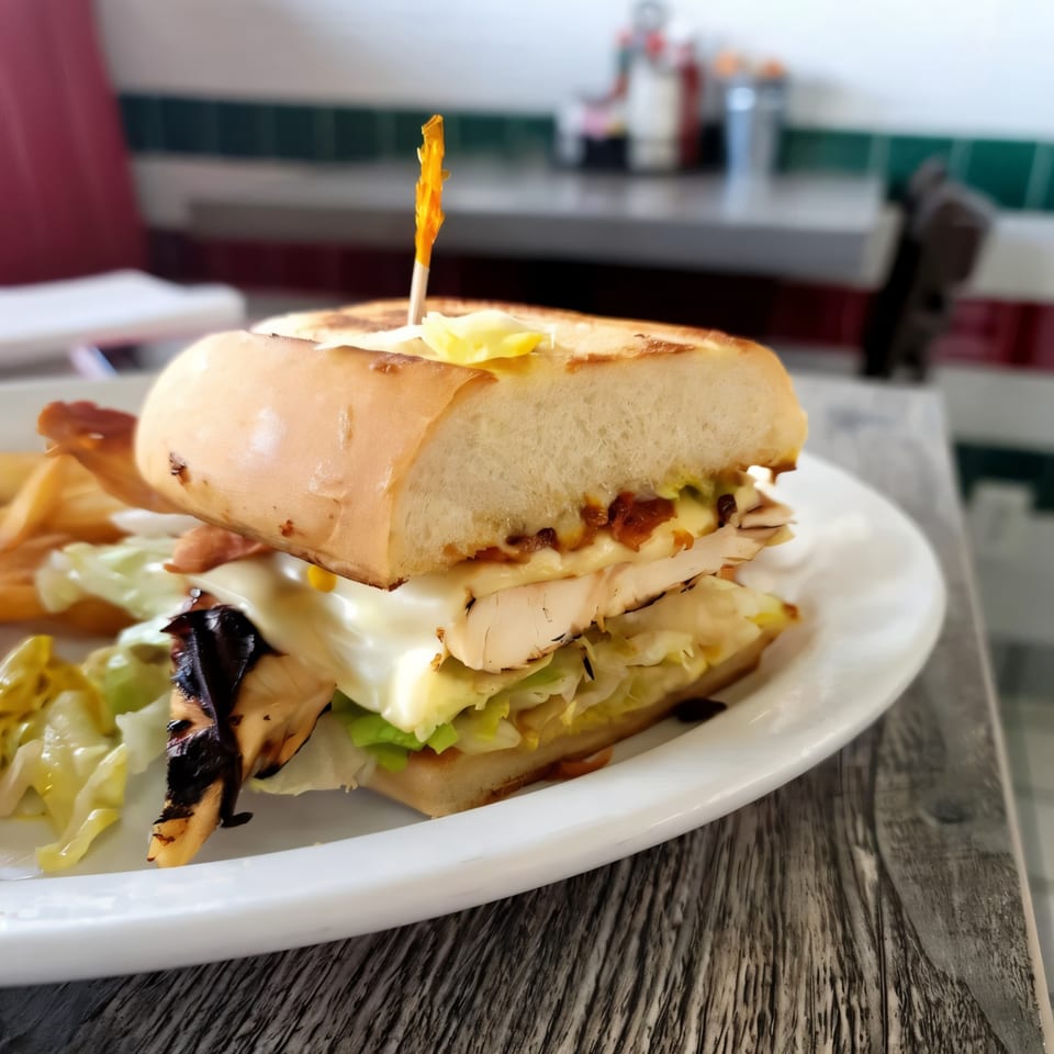 A grilled chicken sandwich with lettuce, cheese, and sauce on a white plate at Jerry's Cafe.
