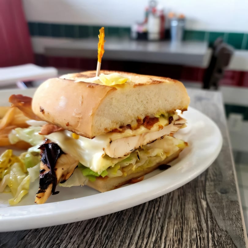 A grilled chicken sandwich with lettuce, cheese, and sauce on a white plate at Jerry's Cafe.