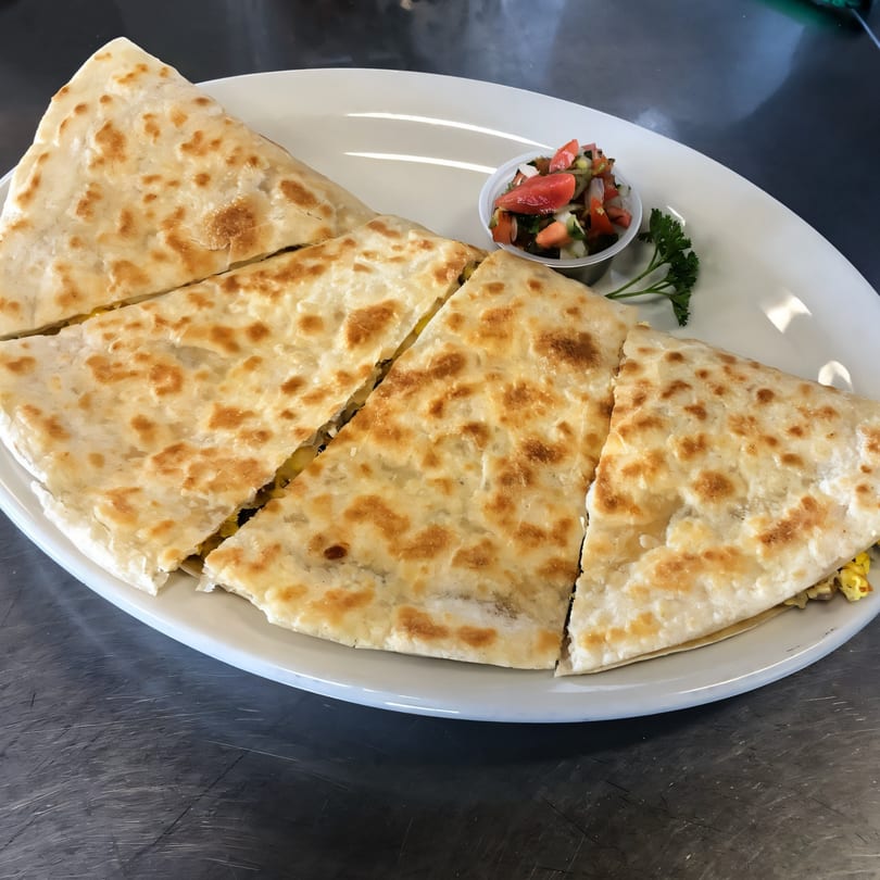 A large quesadilla, cut into four triangles, served with a side of salsa and parsley.