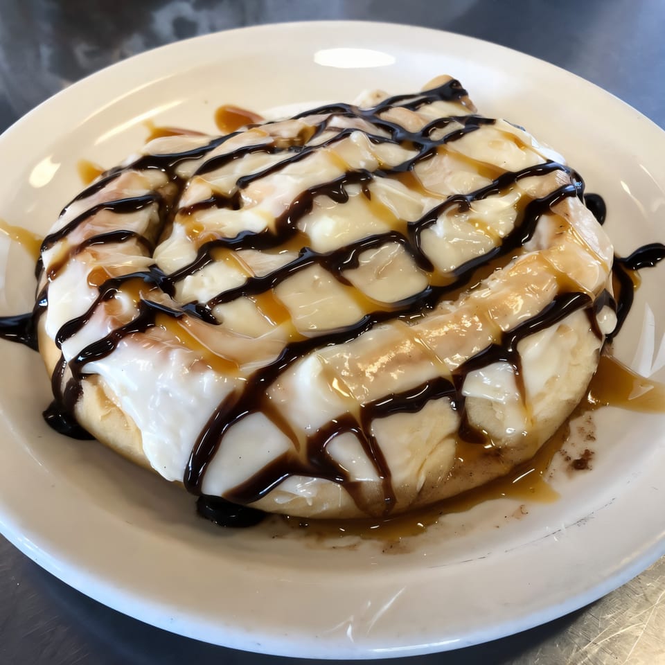 A large cinnamon roll from Jerry's Cafe, topped with white icing, chocolate, and caramel drizzle.